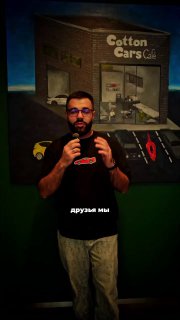 Мужчина в очках говорит на фоне оформления Cotton Cars Cafe: логотип и иллюстрация машин на тёмной стене, кадр из сторис.