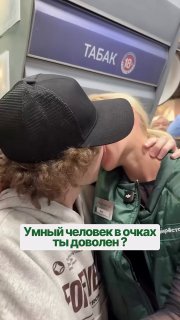 Момент поцелуя в общественном транспорте: мужчина в чёрной кепке целует партнёра в очках и бейджике, на заднем плане видна табличка «ТАБАК».