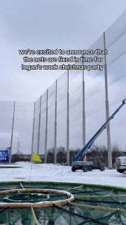 Открытая площадка Topgolf зимой: вид на игровое поле и высокие опоры с сеткой; кадр на фоне техники, ремонтирующей конструкцию после инцидента.