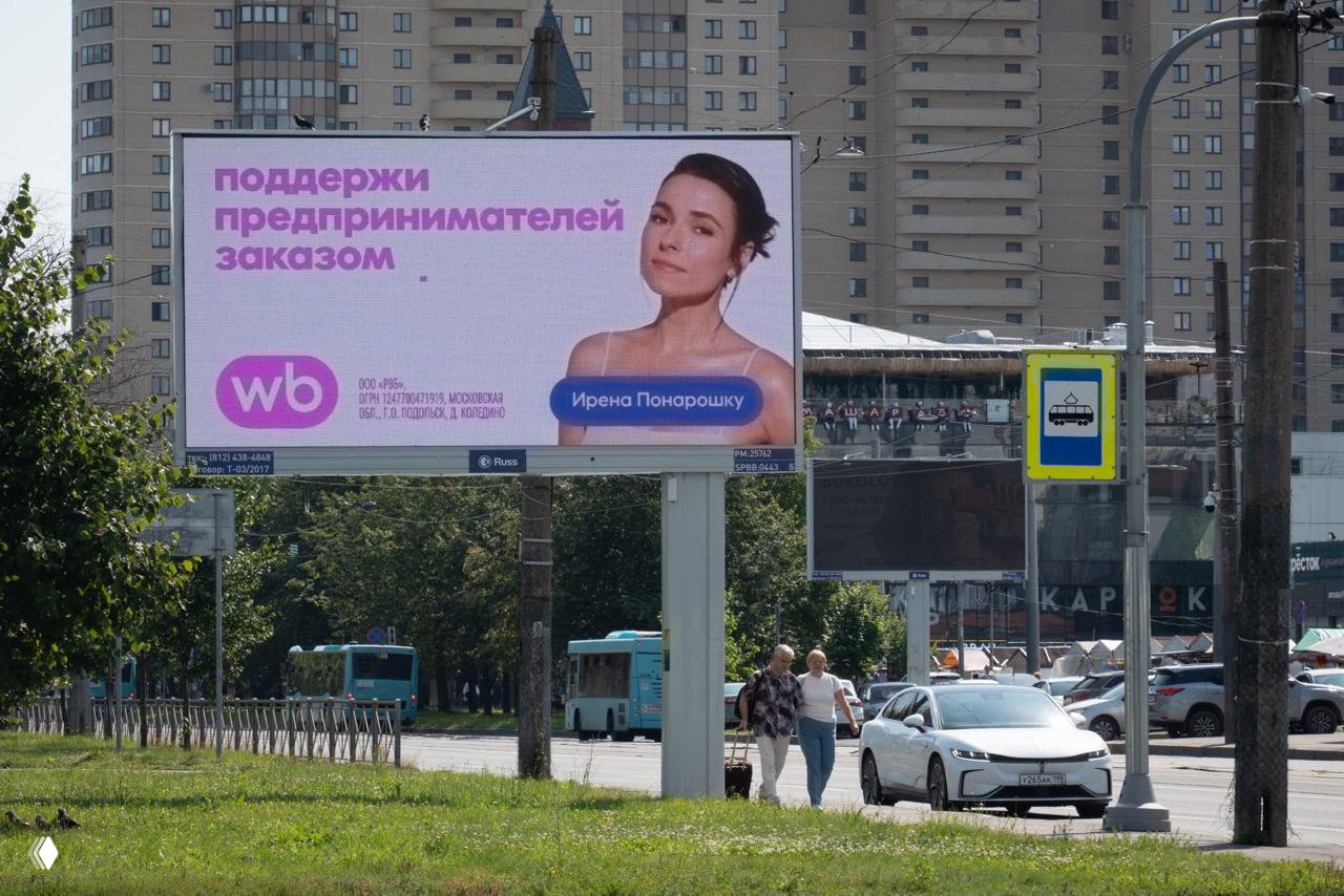 Рекламный щит Wildberries с изображением Ирэны Понарошку и слоганом «поддержи предпринимателей заказом» на фоне домов и городской улицы