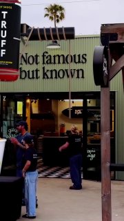 Кадр рекламного ролика: фасад пекарни PopUp Bagels с большой вертикальной вывеской TRUFF, у входа несколько людей и видно интерьер на заднем плане