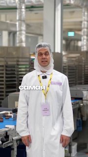 Мужчина в белой производственной форме и шапочке на конвейерной линии упаковки снеков; заводской цех на фоне, иллюстрация к теме бренда.