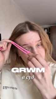 Девушка в кадре GRWM-бьюти-видео держит розовый инструмент у лица, снимает макияж/уход в вертикальном формате.