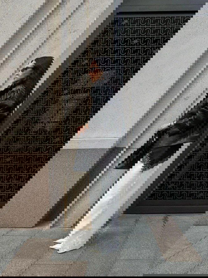 Стритстайл: женщина в чёрной кожаной куртке и белых брюках, с кружевной тонкой юбкой‑слоем снизу — контраст текстур и стилей.