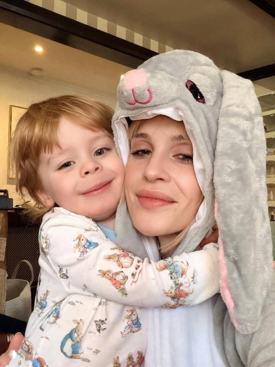 Крупный портрет: взрослая и ребёнок в мягком костюме-зайце обнимаются; тёплые выражения лиц и уютный домашний фон на снимке.