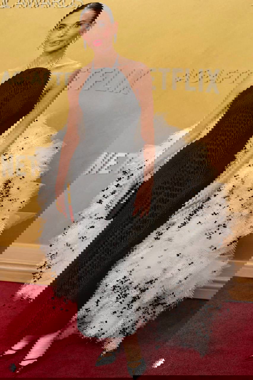 Тонкая фигура в чёрном платье с экстравагантной объёмной белой тюлевой деталью позирует у фонового логотипа SAG.