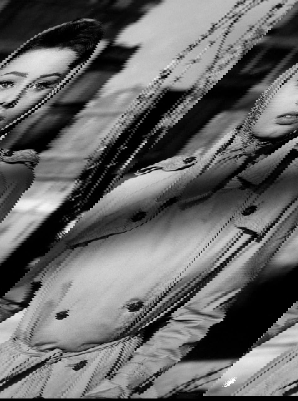 Чёрно-белый портрет женщины в тренче с платком на голове, винтажный образ в кинематографическом стиле, акцент на воротнике, пуговицах и выражении лица.