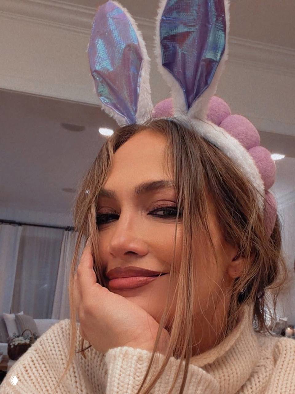 Крупное селфи женщины в ободке с зайчьими ушками; мягкий макияж, тёплый свет и домашняя обстановка в кадре создают уютный портретный образ.