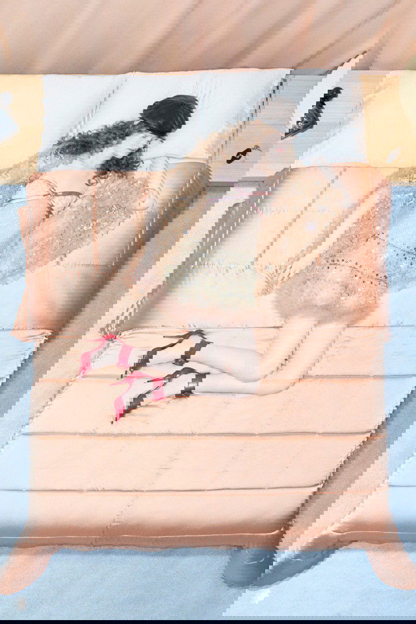 Вид сверху: модель в светлом наряде и красных туфлях лежит на кровати — ещё один образ из круизной кампании Valentino.