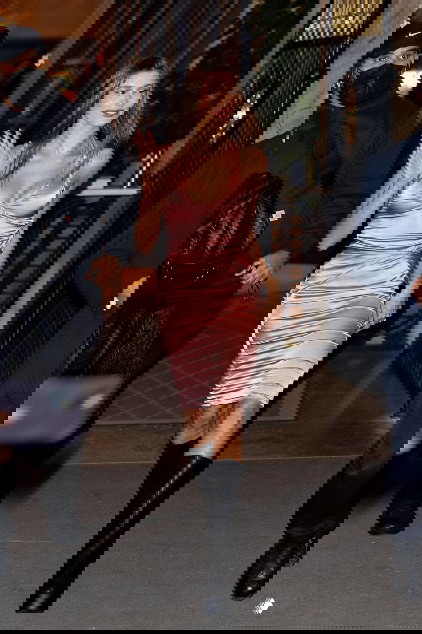 Женщина в облегающем платье и высоких сапогах выходит из здания ночью, снимок подчёркивает гламурный и соблазнительный силуэт.