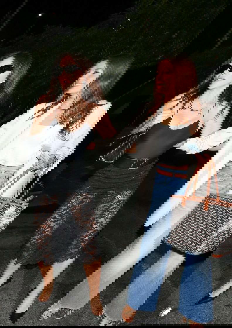 Ева Лонгория и Лорен Санчес идут по тротуару вечером: Лонгория в чёрной кружевной юбке, Санчес в широких джинсах и светлом пиджаке, папарацци рядом.