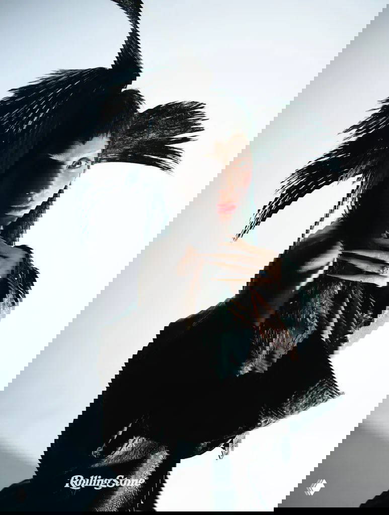 Крупный план лица с художественным макияжем и светлыми бровями, рядом красные цветы — выразительный студийный портрет.