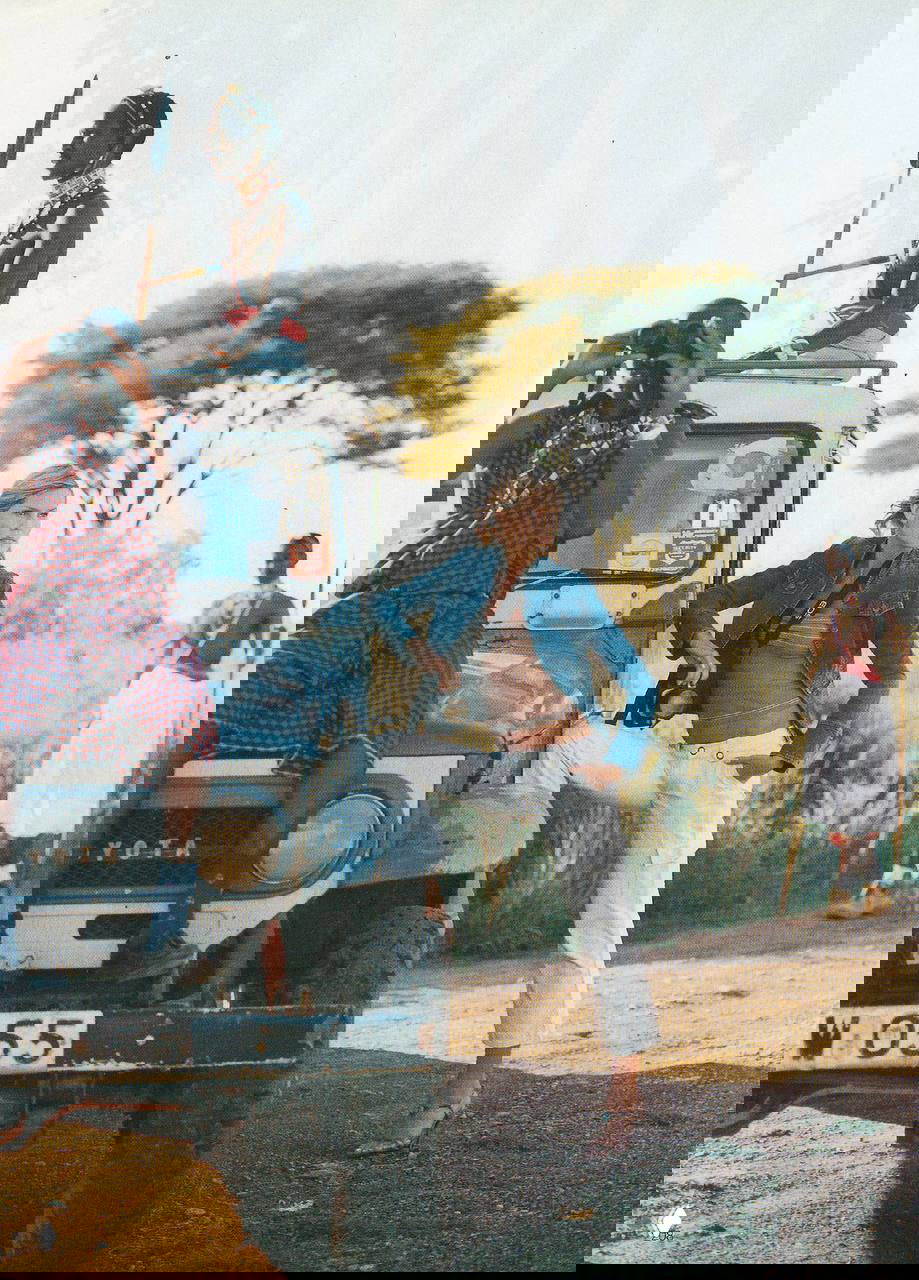 Сафари-кадр с моделью у внедорожника и местных жителей: джип на бездорожье, массаевый антураж и пейзаж саванны в съёмке.