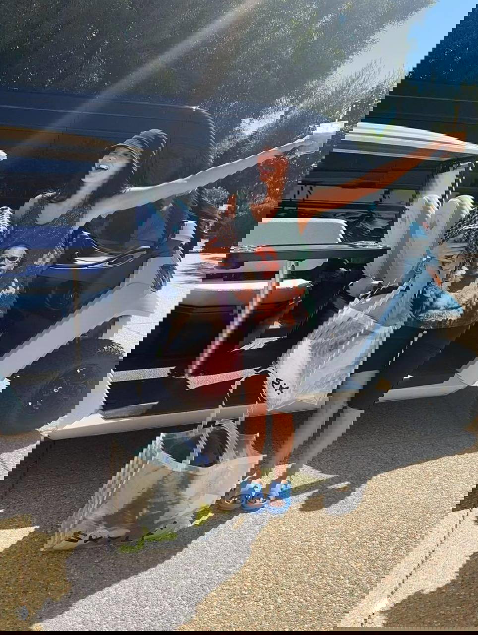 Гость фестиваля рядом с гольф-каром держит прозрачные сумки с вещами и стакан с напитком — повседневная сцена за кулисами события.