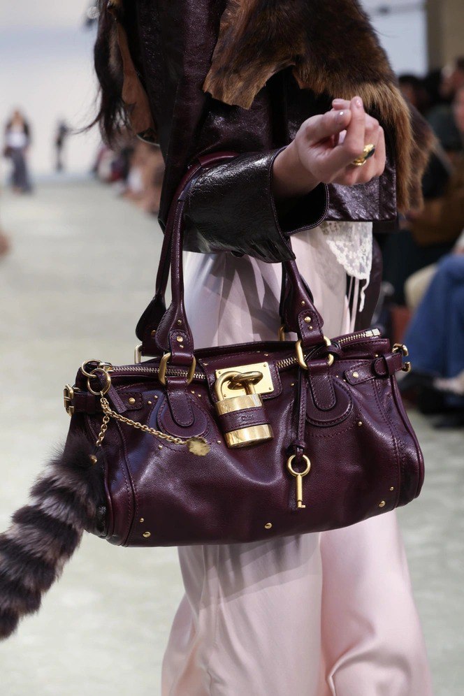 Крупный план бордовой (винной) сумки Chloé Paddington на подиуме с золотым замком и цепочной подвеской, видна текстура кожи