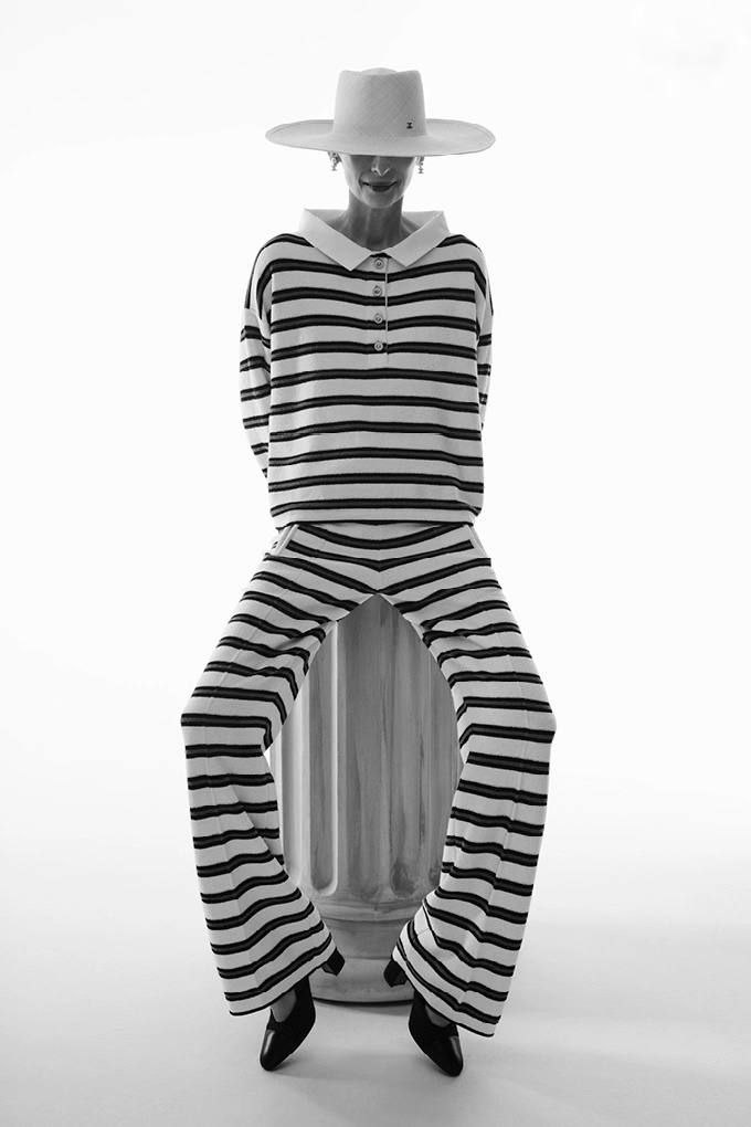 Модель в широком полосатом костюме и шляпе в студийной съёмке; крупные горизонтальные полосы и контрастный свет подчёркивают силуэт.