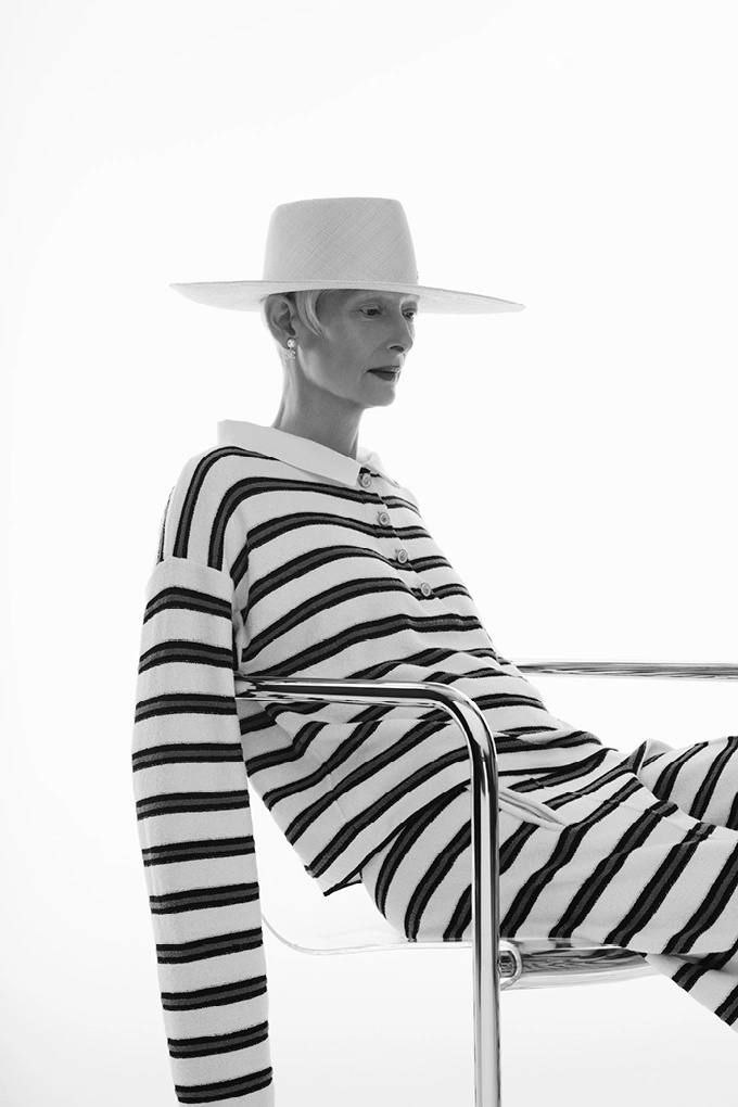 Крупный студийный портрет в профиль: полосатый свитер и брюки, минималистичная шляпа и чистый свет создают сдержанную эстетическую картину.