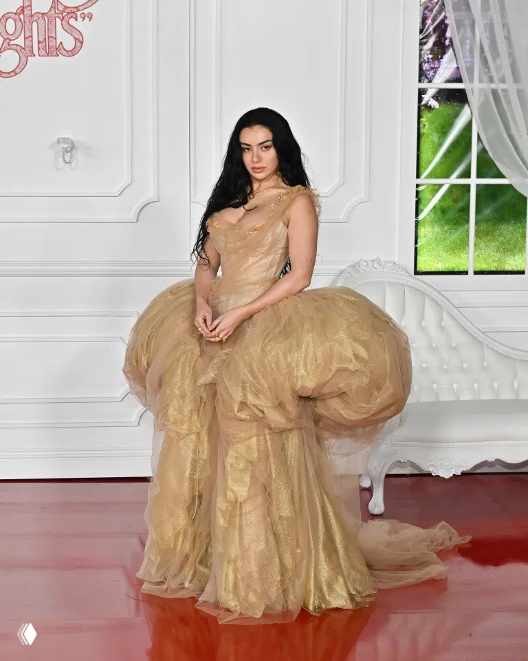 Женщина в пышном золотистом платье с объёмной юбкой позирует на глянцевом красном полу у белого интерьера, образ в стиле высокой моды.