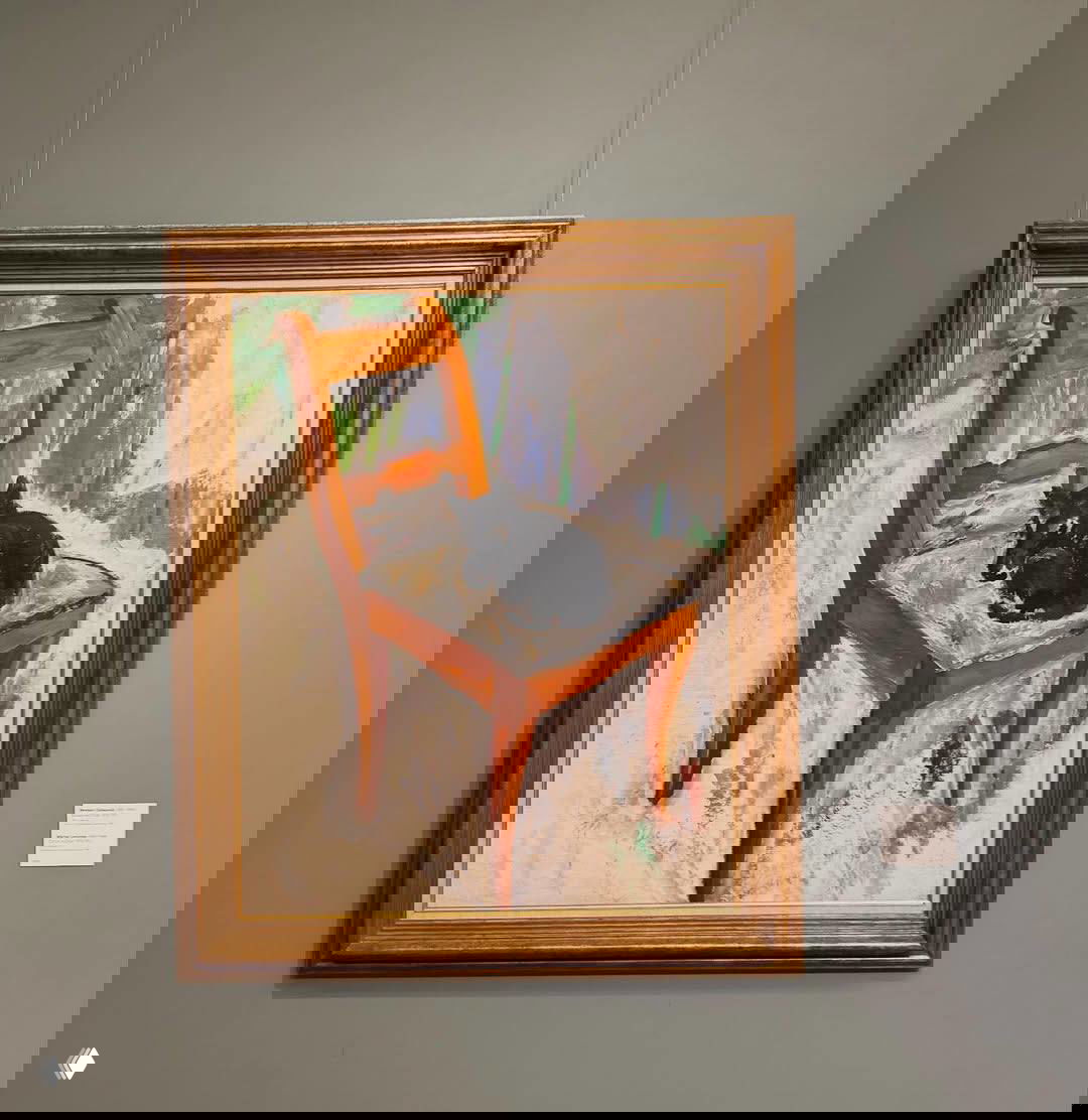 Полотно с изображением деревянного стула и спящего чёрного кота на сиденье в декоративной золотой раме на нейтральной музейной стене.