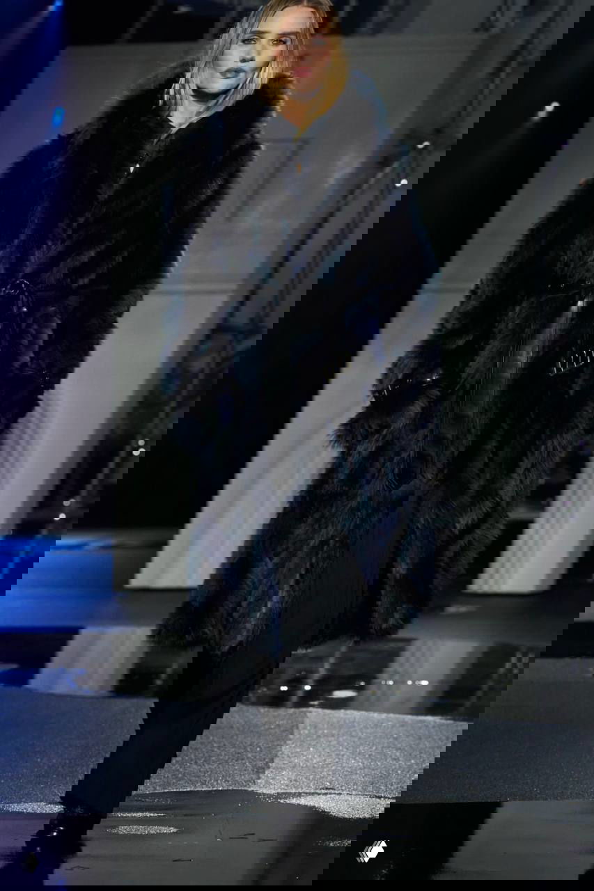 Модель в пышной шубе глубокого бордово‑тёмного оттенка на фоне мокрого подиума и арочной декорации шоу Burberry в Лондоне.