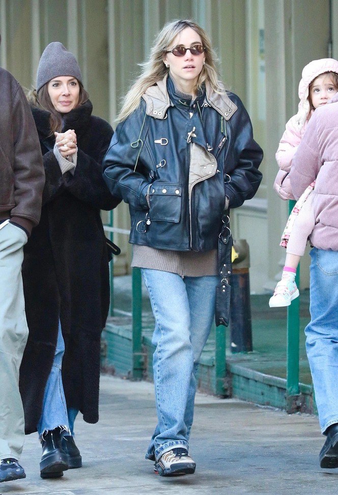 Городской стритстайл: женщина в тёплой кожаной куртке, свободном свитере и голубых джинсах идёт по тротуару рядом с прохожими.