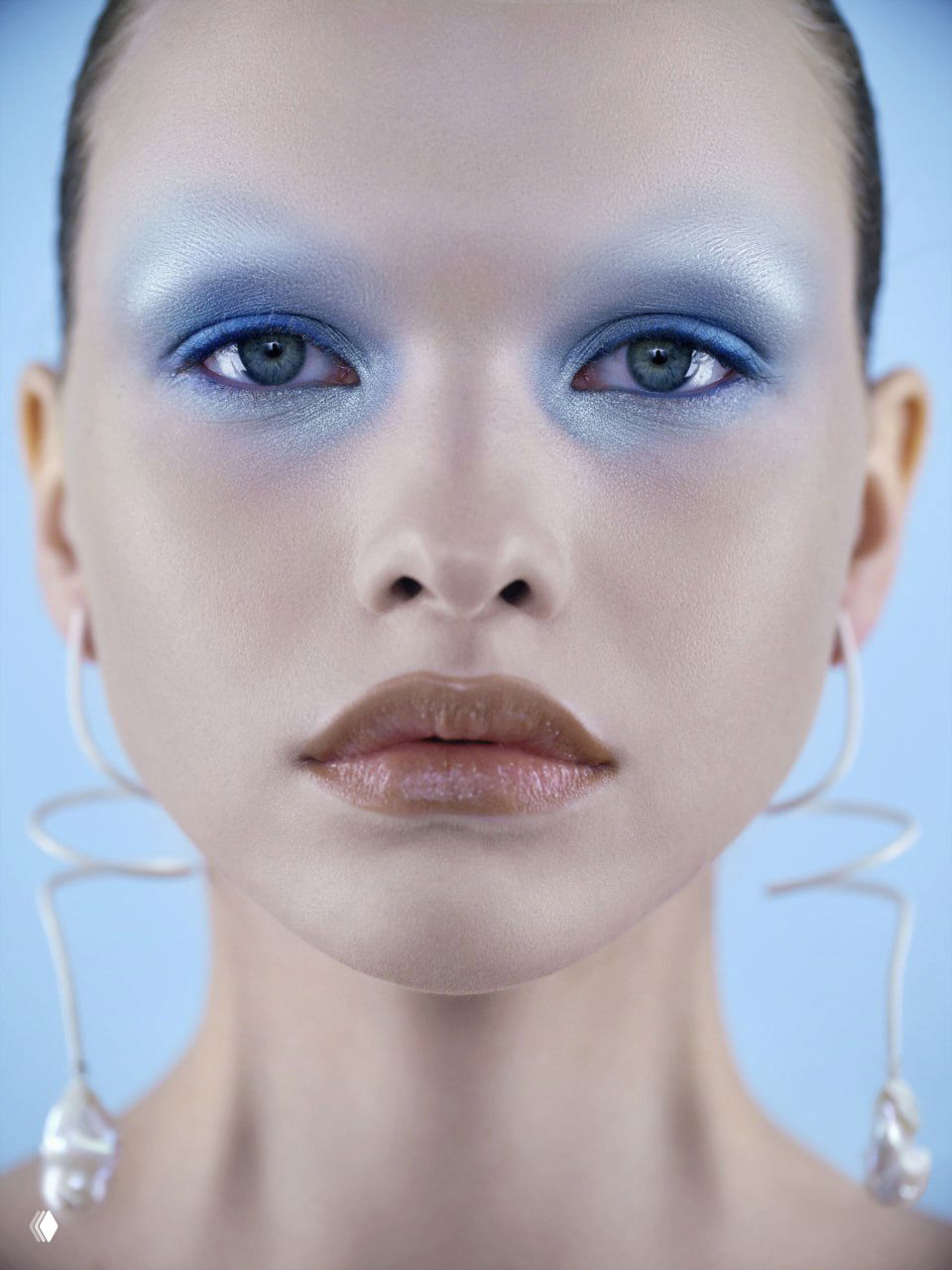 Фронтальный портрет с глубоким макияжем 'лагуна': насыщенные синие тени вокруг глаз, ровная кожа и крупные дизайнерские серьги на голубом фоне.