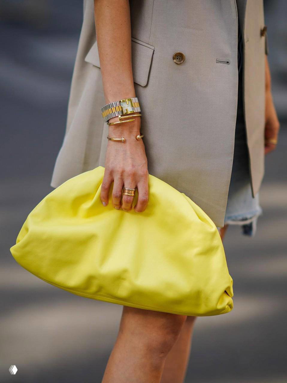 Крупный план руки с несколькими золотыми браслетами и крупной жёлтой сумкой; модный стритстайл и акцент на аксессуарах.