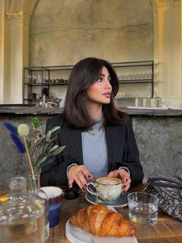 Девушка в кафе с чашкой кофе и средней длиной волос, аккуратно уложенными в классический боб с лёгкой чёлкой‑занавес.