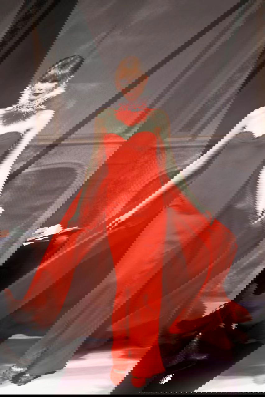 Модель в ярком красном платье с развевающимся шлейфом и перьевым воротником; эффектный праздничный образ Valentino, 1998.