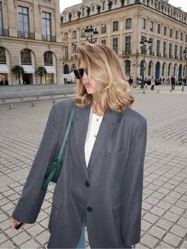 Женщина на улице в пиджаке с объёмной стрижкой до плеч — пример мягкого каскада и естественного объёма для весны.