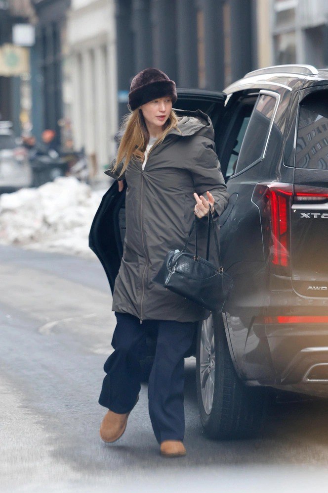 Зимний повседневный кадр: женщина в тёмном пуховике с капюшоном и шапке выходит у автомобиля, на улице видны сугробы и лёд.