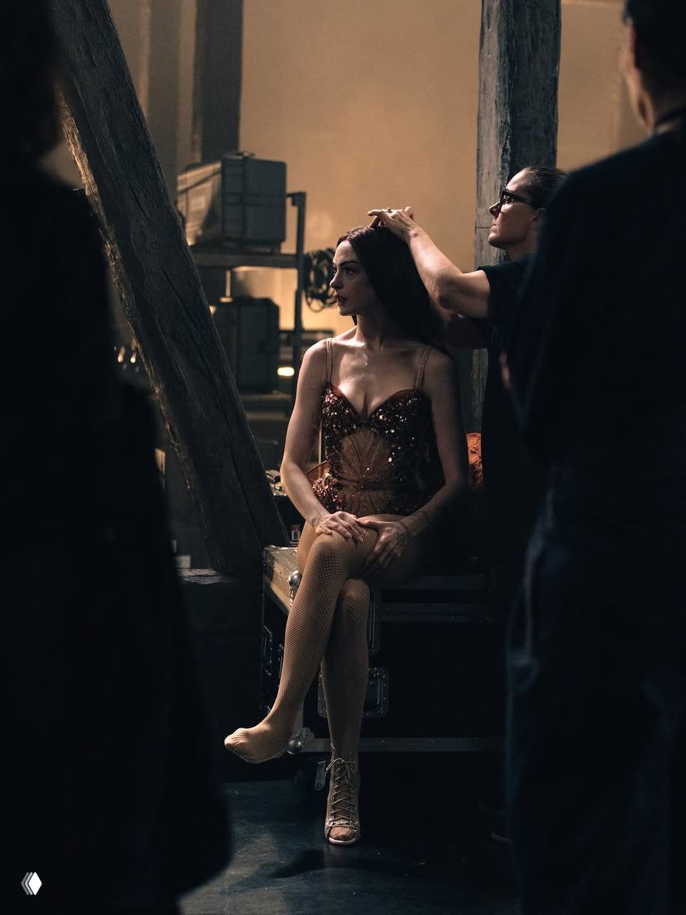 Актриса сидит в гримёрной на съёмочной площадке в корсетном, блестящем костюме; подготовка к сцене, стилист поправляет причёску и свет