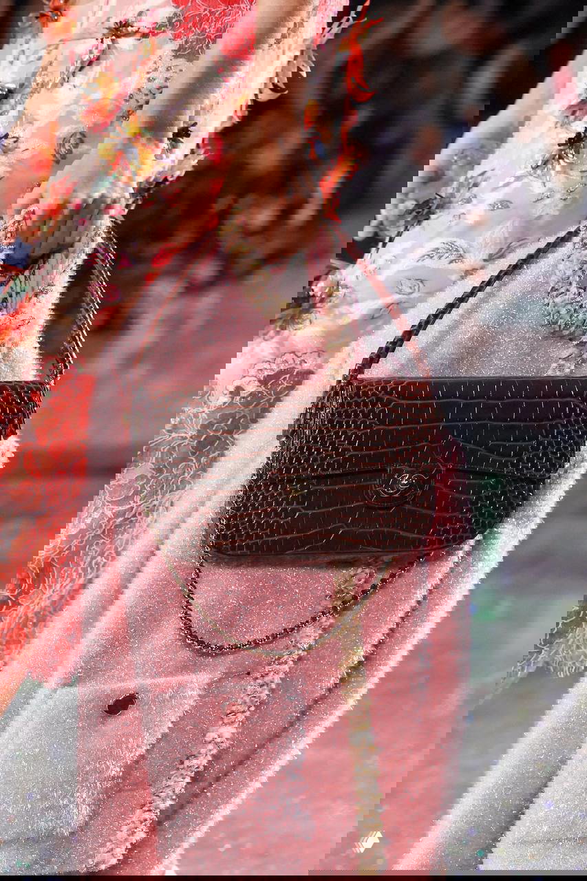 Коричневая мини-сумка с крокодиловым тиснением от Chanel у модели в розовом образе на подиуме: цепочка, структурированная форма и твидовый фон.