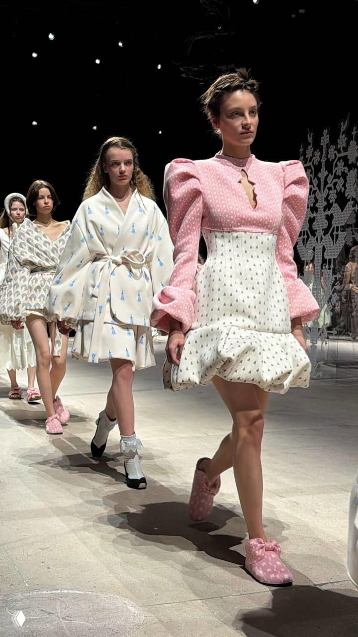 Группа моделей в пастельных и белых силуэтах с объёмными рукавами и принтами идёт по подиуму — атмосфера семейной эстетики коллекции.