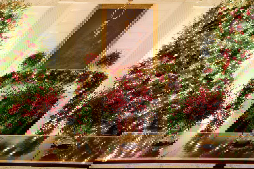 Каминный зал Белого дома украшен цветочными композициями и двумя большими ёлками по бокам, праздничные гирлянды подчёркивают архитектуру комнаты.