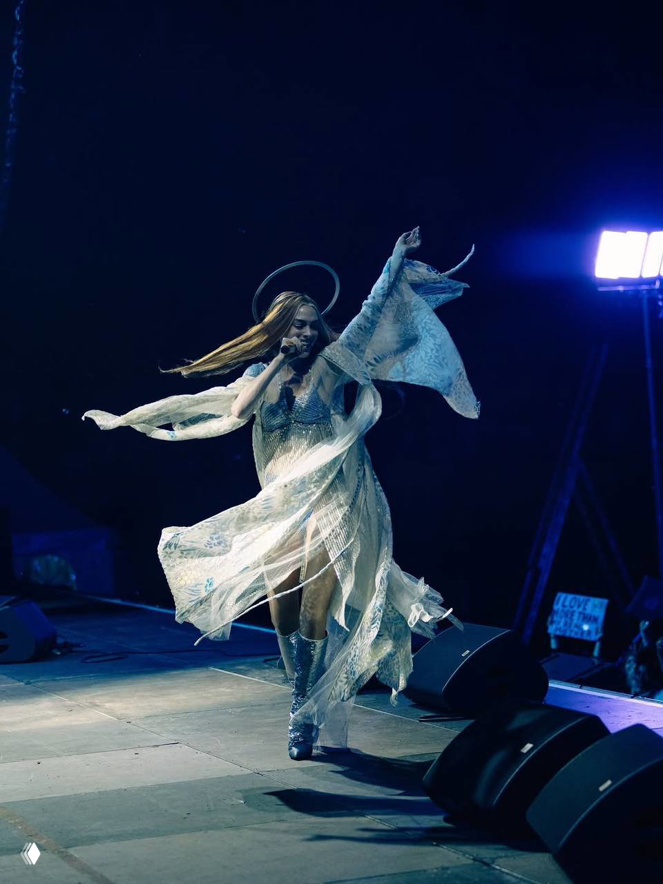 Энн в воздушном, развевающемся наряде на сцене во время выступления; широкая сцена, мощное сценическое освещение и динамика движения