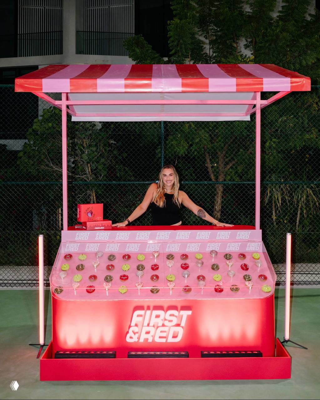 Стенд First&Red в розовых и красных тонах: Арина стоит за витриной с пончиками, фотозона вечернего мероприятия на открытом воздухе.