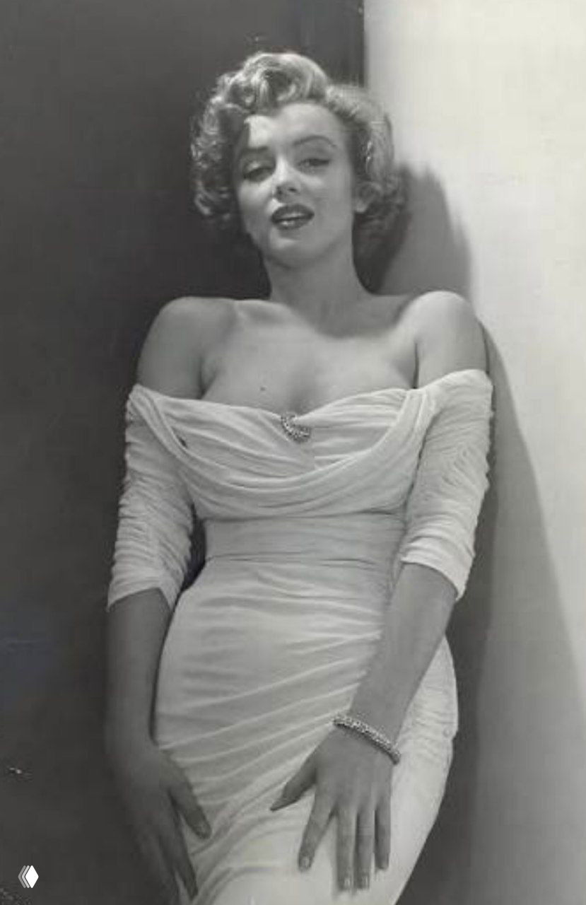 Чёрно‑белая ретро‑фотография женщины в молочном платье 50‑х с характерной драпировкой и браслетом на руке, студийный кадр.