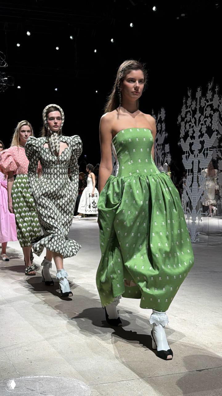 Группа моделей, в том числе в зелёном платье с пышным силуэтом, закрывает показ; заметны кружевные мотивы и ретро‑узоры коллекции.