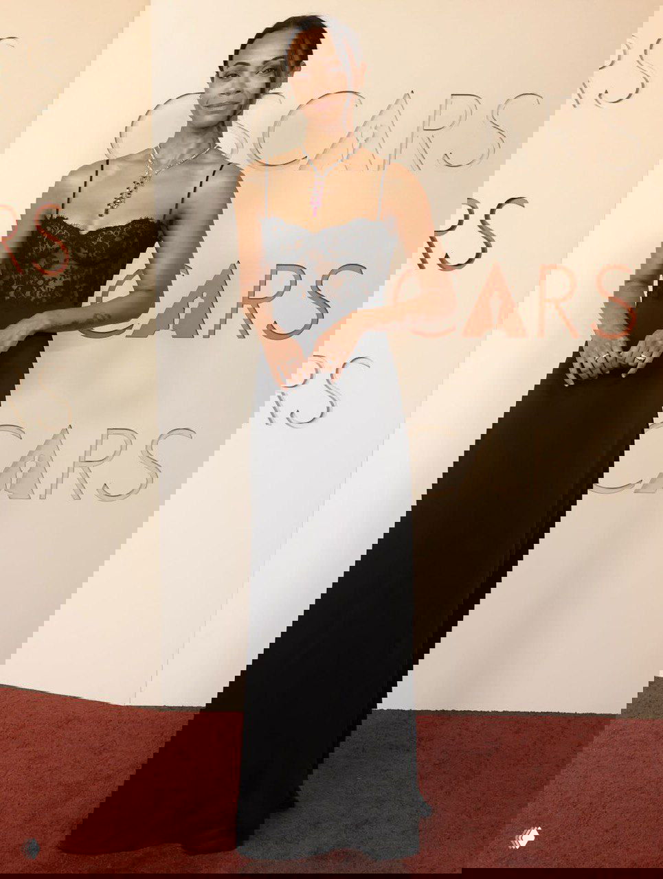 Женщина в минималистичном чёрном платье с тонкими бретелями на красной дорожке Оскара 2026, вертикальный портрет в полный рост.