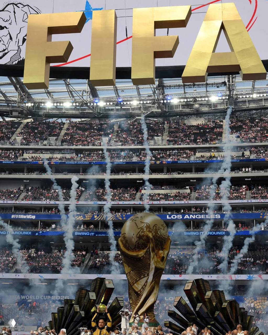 Панорамный вид стадиона с большой инсталляцией FIFA и трофеем на поле, пиротехника и заполненные трибуны во время церемонии открытия.