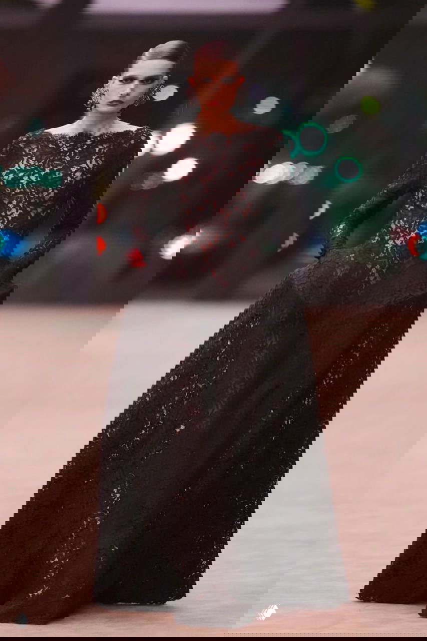 Модель в длинном чёрном кружевном платье на подиуме Saint Laurent, выразительный макияж и крупные серьги в кадре.