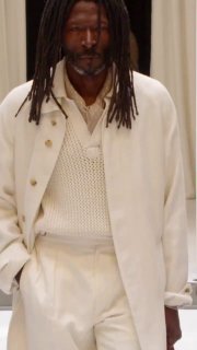 Модель в белой вязаной жилетке и светлом пальто на подиуме показа Ralph Lauren; образ сочетает текстуры и классический силуэт в мужской коллекции.