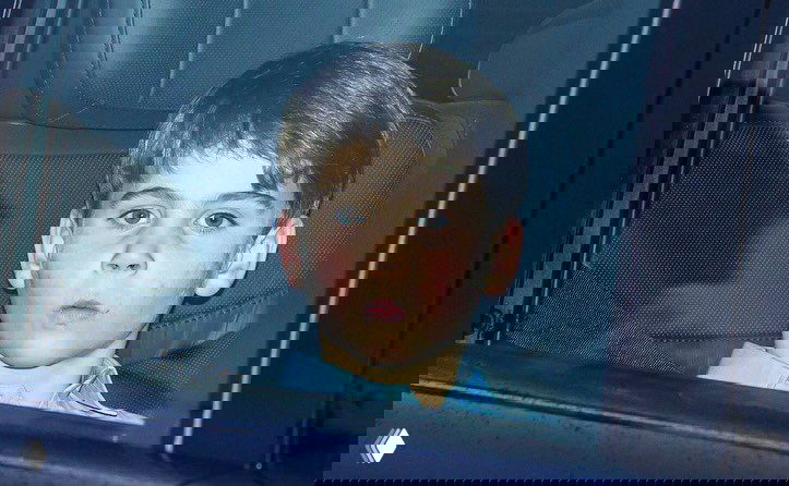 Мальчик в салоне автомобиля смотрит в сторону, кадр папарацци через окно во время перемещения семьи по городу вечером.