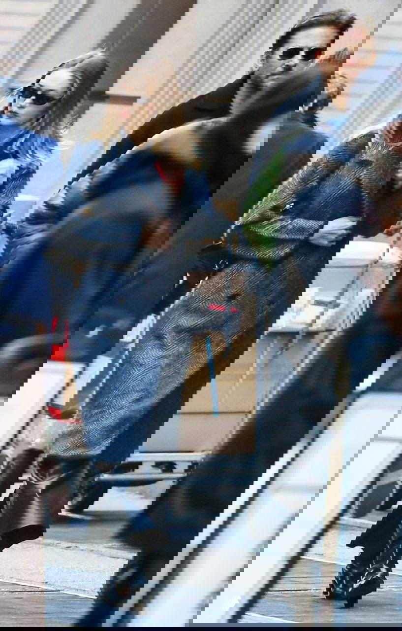 Женщина в длинном двубортном пальто тёмного оттенка и кожаных брюках, уличный кадр в городской суете — строгий лаконичный стрит-стиль.