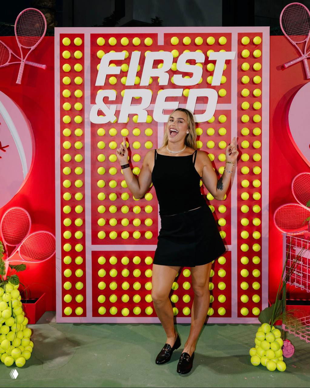 Арина Соболенко позирует у яркой инсталляции с логотипом FIRST&RED и множеством теннисных мячей — вечерняя рекламная фотозона в Дубае.