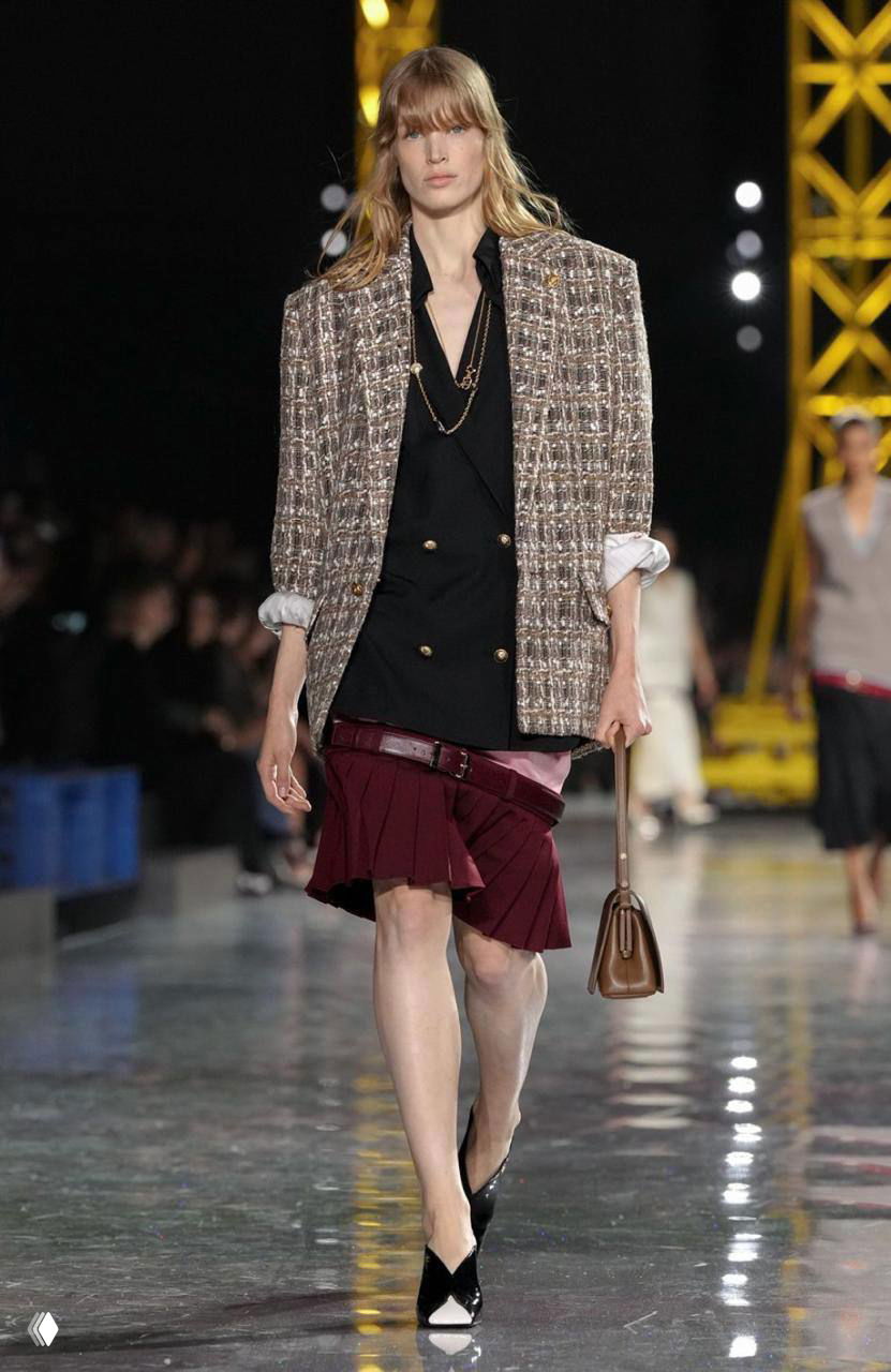 Модель в твидовом пиджаке и юбке с ремнем на бедрах выходит на подиум Chanel; комбинация твида и ременных акцентов возвращается из архивов бренда.