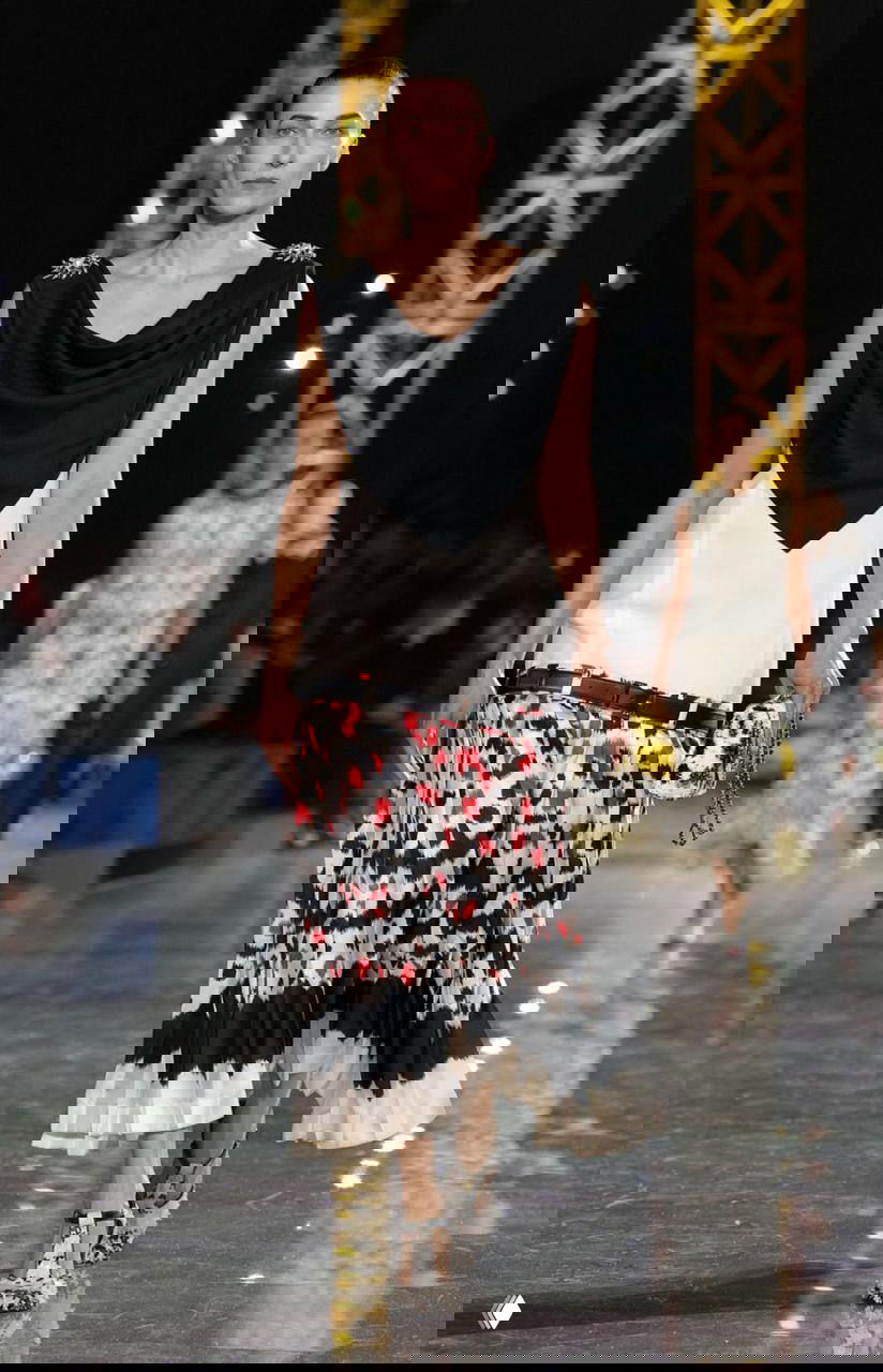 Модель в контрастном чёрно‑белом образе с принтованной плиссированной юбкой и ремнем на бедрах демонстрирует тренды сезона на показе Chanel.