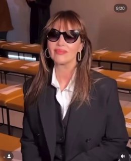 Женщина в солнцезащитных очках на переднем плане в зале показа: ряды с местами и подготовка сцены перед началом дефиле, интерьер fashion-шоу.