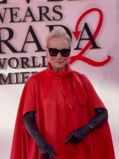 Крупный кадр с красной дорожки: женщина в красном на фоне баннера премьеры, длинные рукава и солнцезащитные очки создают драматичный образ.